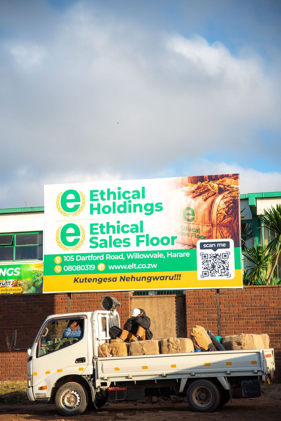 A truck loaded with tobacco bales and crew parked below the Ethical Sales Floor billboard